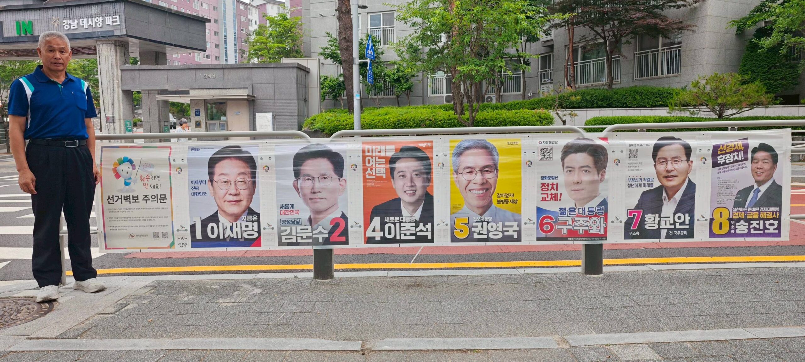 葉竹林於李在明擔任8年市長的城南市的社區投票所外與總統候選人競選海報欄合影。(圖/取自葉竹林臉書)